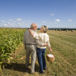 Senior couple standing next to a cornfield embracing and smiling at each other.