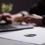 Person working on a laptop computer backlit with paperwork in the foreground.