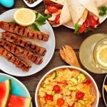 Summer food on wooden table, including pasta salad and BBQ grilled skewers.