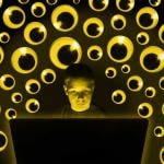 Photo illustration of student at laptop surrounded by many pairs of googly eyes watching; surveillance concept.
