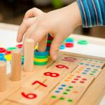 Child playing with different color wooden rings on a board with painted numbers and dots.