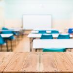 View of empty classroom with desks and blue chairs chairs and whiteboard.