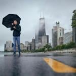 A person with an umbrella walks against the Chicago cityscape on a rainy, windy day.