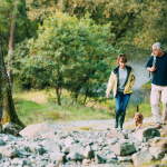 Senior couple walking through the woods with their pet dog.