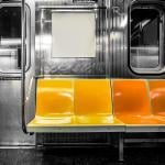 A black and white photograph inside a subway train but the seats are colored in yellow and orange.