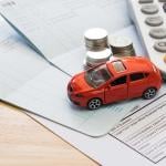 Car insurance bills are seen with a red toy car, coins and a calculator on top of it.