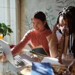 Two Gen Z women are engaged in a discussion while using a laptop.