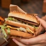 Double cheeseburger in customer's hands at fast-food restaurant.