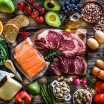 Overhead view of protein-rich foods including red meat, salmon, cheese and a wide range of fruits and vegetables.