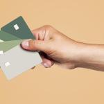 A person's hand is holding four credit cards displayed over a beige background.