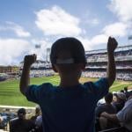 A young boy cheering inside a baseball stadium while facing the field.