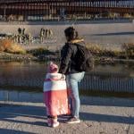 View of woman and child from behind on Ciudad Juarez side of border with border agents visible across the river. 