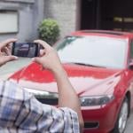 Young person in foreground taking photo of a red car from the front with a smartphone.