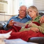 A senior couple sitting together looking worried while reading a bill.