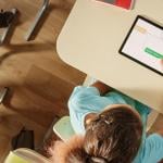 High-angle view of tween student using a tablet on a desk in the classroom. 