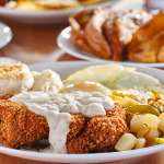 Chicken fried steak covered in gravy with sunny side up eggs, biscuits and potatoes on a plate