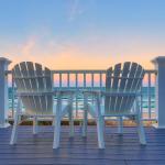 Two coastal style outdoor chairs facing the beac during sunset.