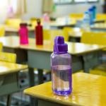 Different colored water bottles sit on yellow desks in a classroom.