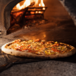 A freshly-baked pizza being pulled out of a wood-fire oven