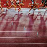 Legs of female track and field athletes running on the track cast long shadows onto the red track during professional 1500 m race.