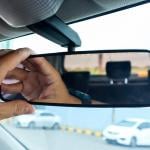 Hand of a driver getting ready for a drive by adjusting rear view mirror of car.