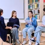 Three teens face sitting in chairs talking with a school counselor in a library setting. 