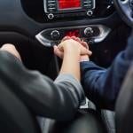 Couple holding hands in car while commuting to work.