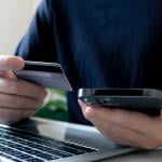 A person holding a credit card, making a purchase payment using a laptop and a phone.