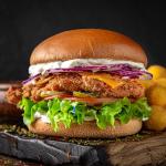 A close-up of a burger sitting on wooden cutting board against a black background.