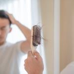 A man looking at his brush with plenty of hair loss.