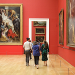 Visitors walk through an exhibition with art on red-orange walls inside Lille’s Palais des Beaux-Arts. 