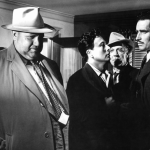 Orson Welles, Charlton Heston and other men gathered in room in a scene from the film 'Touch Of Evil', 1958. 