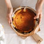 Top view of baker holding basque cheesecake in baking paper.