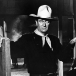 American actor John Wayne (1907 - 1979) wears a Western outfit which includes a pistol in a holster and stands in a doorway in a still from the Cowboy film 'The Man Who Shot Liberty Valance' directed by John Ford, 1962.