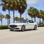 White Genesis G90 on the road with palm trees and sky in the background.