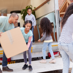 Family unpacks cardboard boxes from moving truck.