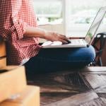 A female small business owner with boxes behind her using a laptop.