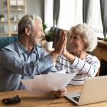 A baby boomer couple giving each other high five while doing finances.