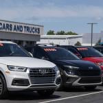 A row of cars in a dealership lot with a signage saying "used cars and trucks" in the background.