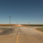 A rural intersection in Texas with a stop sign and a blue sky in the background.