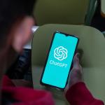 Young person in classroom looking at ChatGPT app on smartphone, seen from behind.