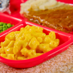 TV dinner with Salisbury steak, macaroni and cheese, and peas on a red tray.