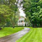 A colonial-style white house at the end of a long driveway in an affluent neighborhood in Madison, Connecticut