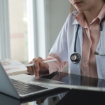 A doctor working on a laptop and using a digital tablet.