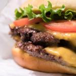 Double cheeseburger in a wrapper with tomato, lettuce, and onion.