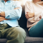 A fighting couple sit apart on a sofa