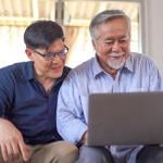 A senior father and his young son looking at information using a laptop at home.