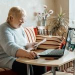 An older woman with disability looking up insurance information online using a laptop.