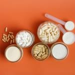 Flatlay of different types of vitamins, supplements and protein powder displayed with an orange background.