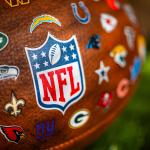 A focus shot on an NFL game ball featuring all logos of NFL teams.